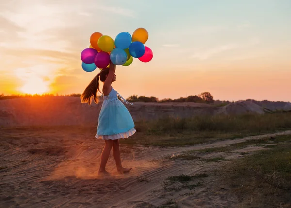 Menina feliz com balões coloridos ao pôr do sol — Fotografia de Stock