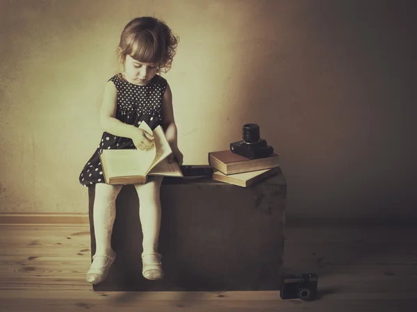 Klein meisje het lezen van een boek op de oude koffer — Stockfoto