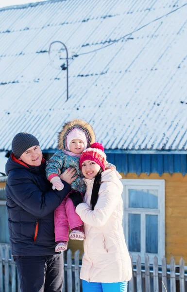 Happy family in warm clothes standing of his house in winter — Stock Photo, Image
