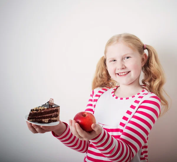 Girl choose from sweet cake and red apple — Stock Photo, Image