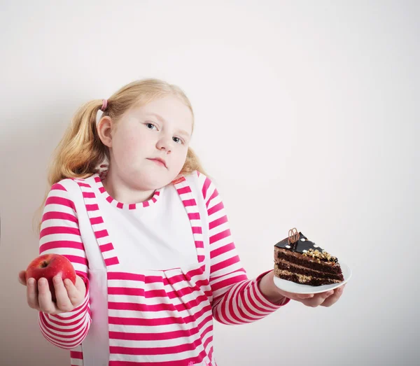Dívka si vybrat ze sladkého dortu a červené jablko — Stock fotografie