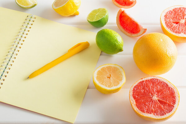 Цитрусовые с ноутбуком на белом деревянном столе
