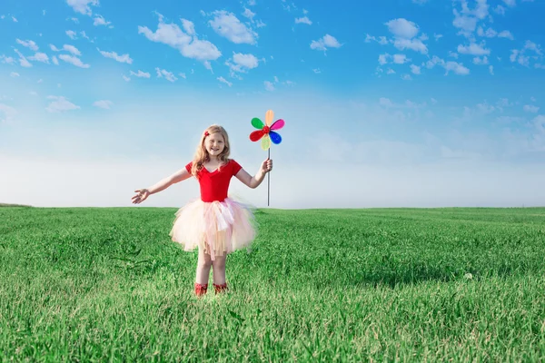 Девушка держит игрушечный цветок на фоне неба и поля — стоковое фото