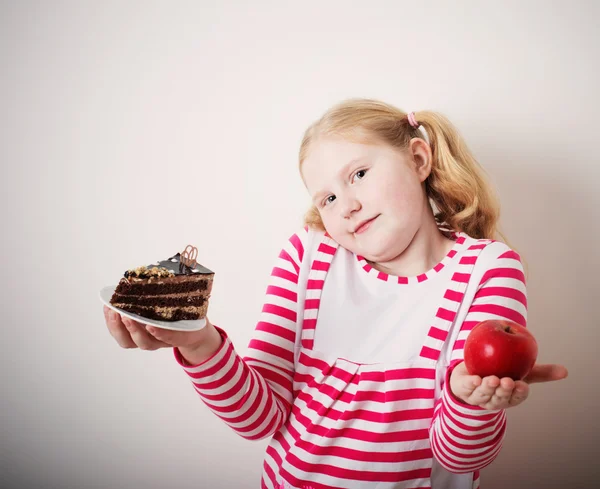 Girl choose from sweet cake and red apple — Stock Photo, Image