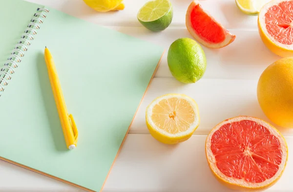 Zitrusfrüchte mit Notizbuch auf weißem Holztisch — Stockfoto