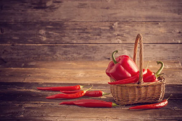 Rode chilipepers in mand op oude houten tafel — Stockfoto