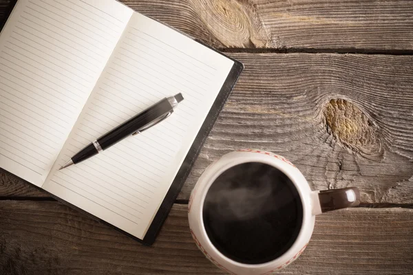 Notebook with pen and coffee on old wooden table — Stock Photo, Image