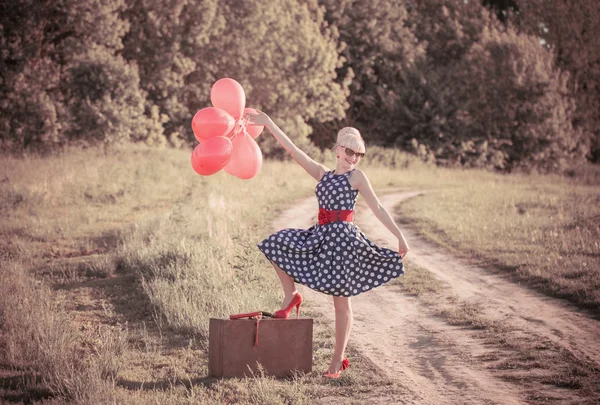 Beautiful girl with suitcase and red balloons at countryside — Stock Photo, Image