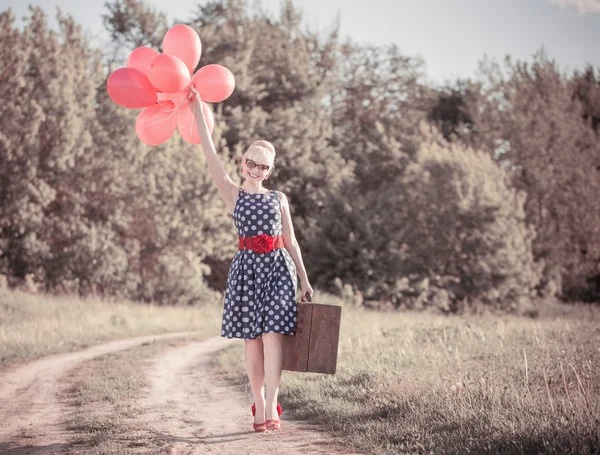 Vacker flicka med resväska och röda ballonger på landsbygden — Stockfoto