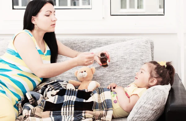 Mother pouring tasty syrup to ease her little girl's cough — Stock Photo, Image