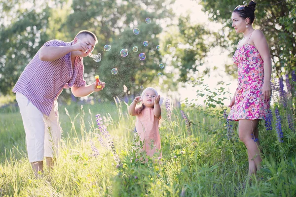 Glad mamma, pappa och dotter blåser bubblor i parken — Stockfoto