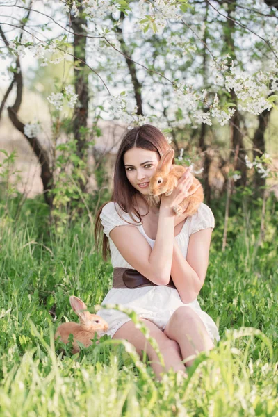 Mooie jonge vrouw met konijnen in tuin — Stockfoto