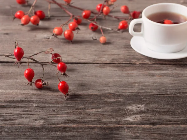 Xícara de chá com rosas da anca, na mesa de madeira — Fotografia de Stock