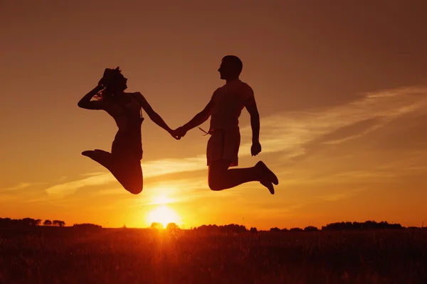 Jovem casal feliz pulando no pôr do sol — Fotografia de Stock