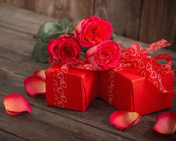 Punainen lahjapaketti ja ruusukimppu puupohjalla — kuvapankkivalokuva