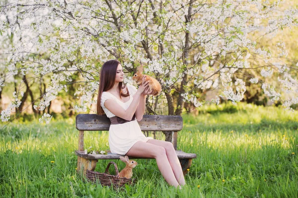 Mooie jonge vrouw met konijnen in tuin — Stockfoto