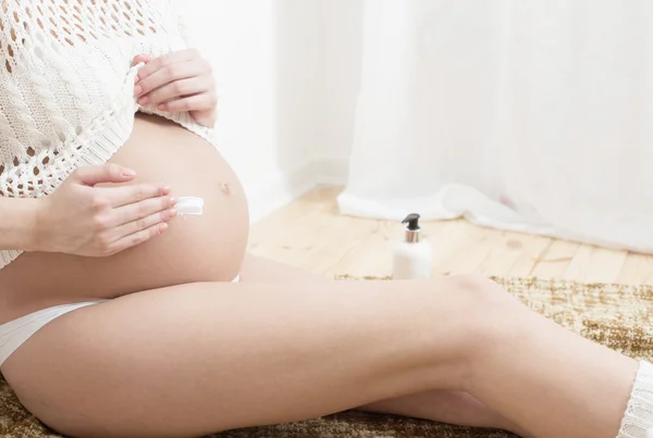 Беременная женщина намазывает крем на живот, чтобы избежать растяжек — стоковое фото