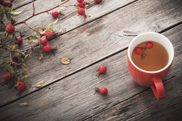 Taza de té con rosas de la cadera, sobre mesa de madera — Foto de Stock