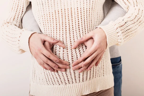 Um casal fazendo uma forma de coração na barriga grávida com seu h — Fotografia de Stock