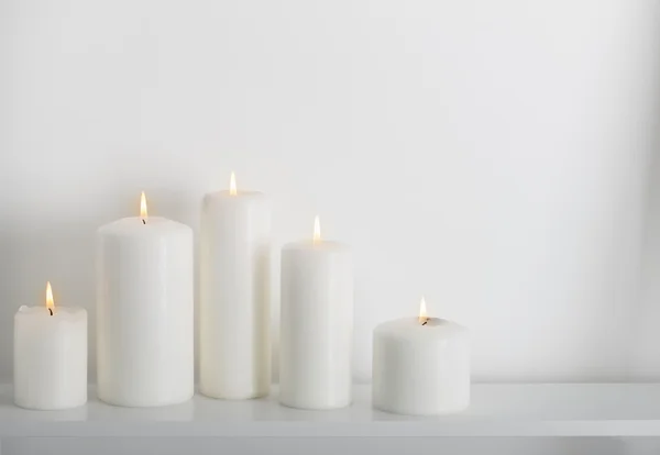 Velas brancas queimando em uma prateleira branca — Fotografia de Stock