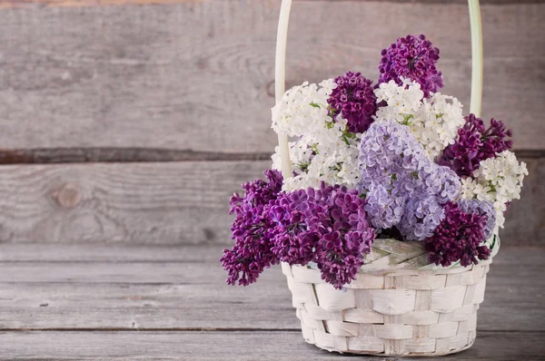 Basket with a branch of lilac flower on a wooden background — Stock Photo, Image