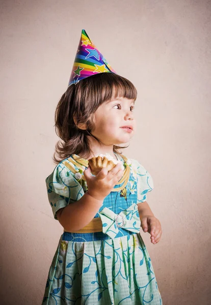 Little girl eating cake in a festive cap in vintage style — Stock Photo, Image
