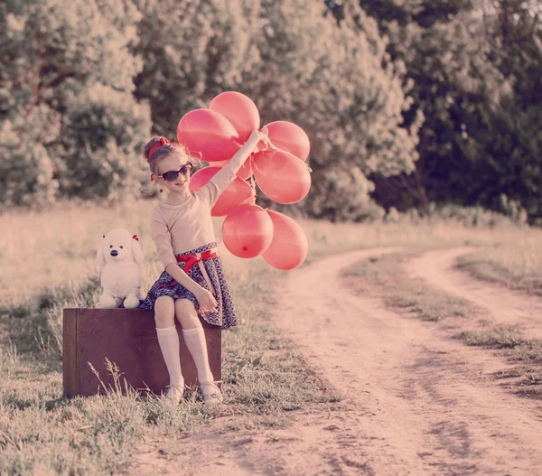 Beautiful girl on suitcase with red balloons outdoor — Stock Photo, Image