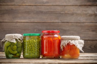 Jars with pickled vegetables on wooden background clipart