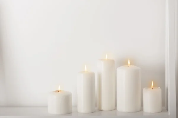 Bougies blanches brûlant sur une étagère blanche — Photo