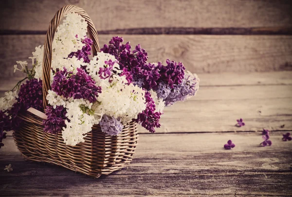 Basket with a branch of lilac flower on a wooden background — Stock Photo, Image