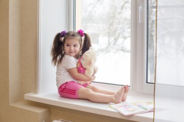 Little happy girl with toy at the window clipart