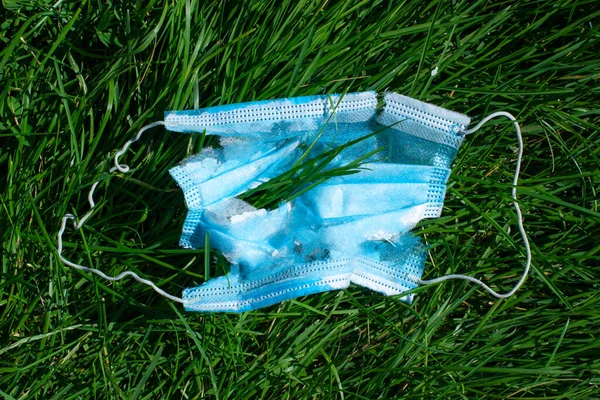 Used disposable medical face mask with holes on green grass. Modern garbage concept.