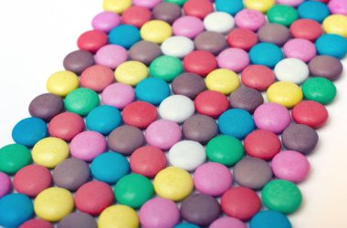 Beyaz zemin üzerinde köşegen yerleştirme desenli renkli şekerler ve sığ alan derinliği