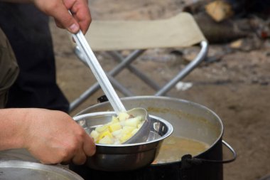 Kamp ateşi üzerine çorba. Tencerede yiyecek ve eğlence