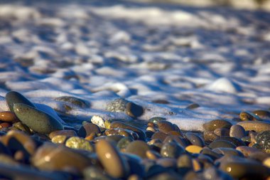 Çok renkli yuvarlak çakıl taşlarının plajı ve tuzlu dalgaların sıçraması. Karadeniz, Kafkaslar