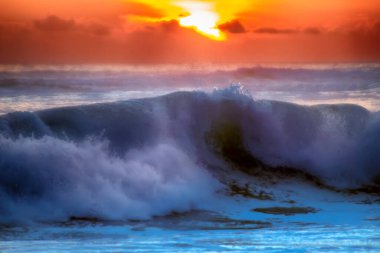 Tropik deniz günbatımının renkleriyle dolu. Dalgalar sahile vuruyor.