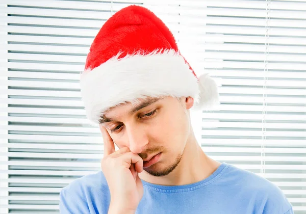Smutný Mladý Muž Santa Klobouk Pozadí Jalousie — Stock fotografie