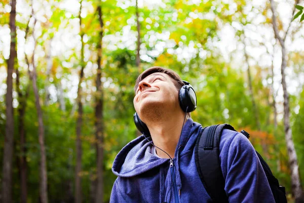 ヘッドフォンの幸せな若者は森の中の音楽を聴く — ストック写真