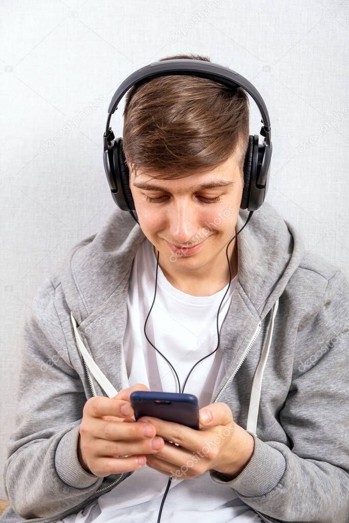 Young Man in Headphones use a Phone on the White Wall Background