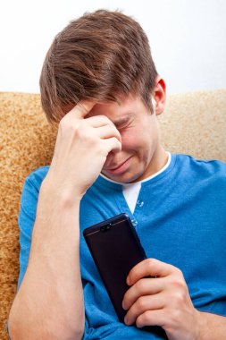 Evdeki koltukta telefonu olan üzgün genç adam.