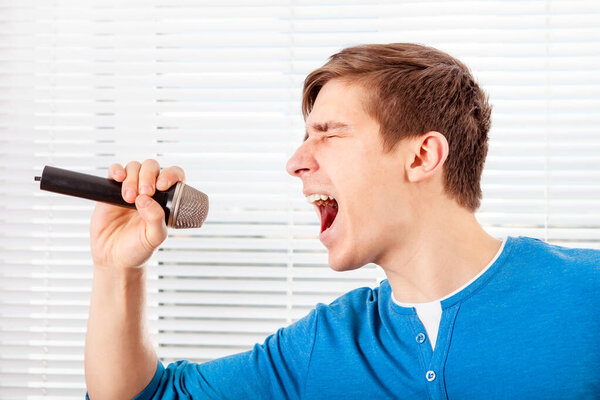 Young Man with a Microphone sing a Song on the Jalousie Background