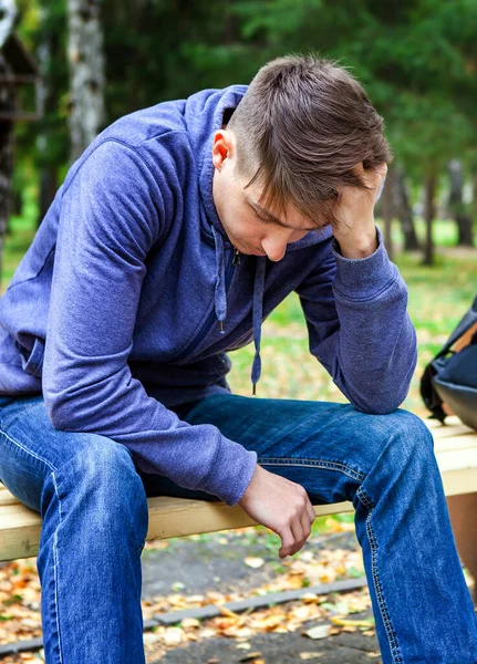 悲哀的年轻人坐在秋天公园的长椅上 — 图库照片