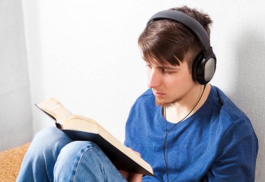 Kulaklıklı genç adam evdeki duvarda bir kitap okuyor.