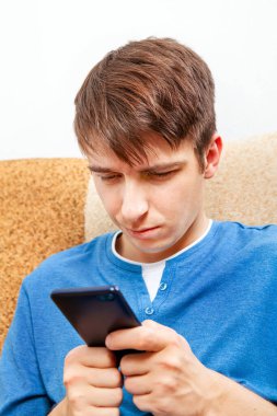 Evdeki koltukta telefonu olan üzgün genç adam.