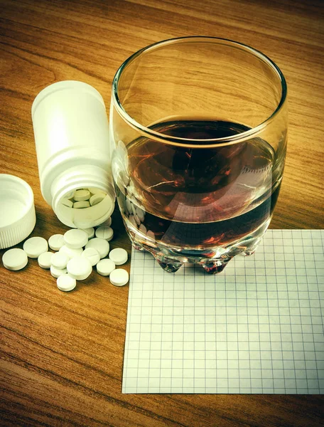 Glass of the Whiskey with a Pills and Empty Paper on the Table closeup