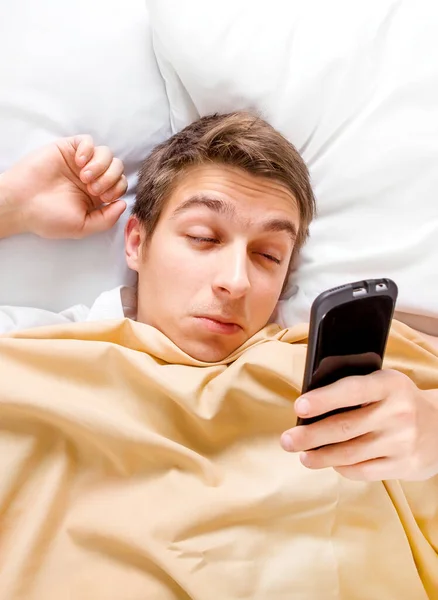 Slaperige Jongeman Wakker Met Een Telefoon Het Bed — Stockfoto