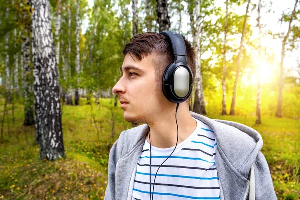 ヘッドフォンの若者が森の中の音楽を聴く — ストック写真