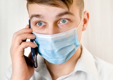 Grip Maskeli Genç Adam duvarın yanında cep telefonu tutuyor.