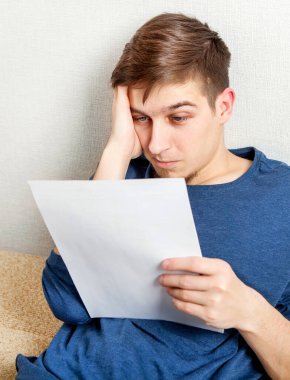 Endişeli genç adam duvarın yanındaki bir belgeyi okudu.