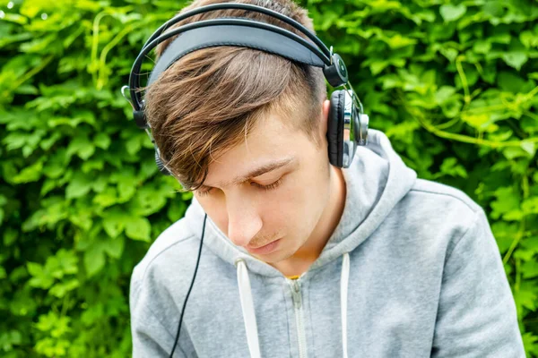Λυπημένος Νεαρός Άνδρας Ακουστικά Στο Πράσινο Αφήνει Φόντο Εξωτερική — Φωτογραφία Αρχείου
